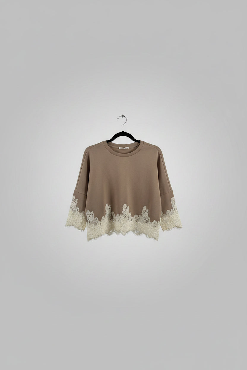 A cropped long-sleeve knit top in taupe brown with a beige floral lace hem and matching lace cuffs, hanging on a black hanger in a retail store.